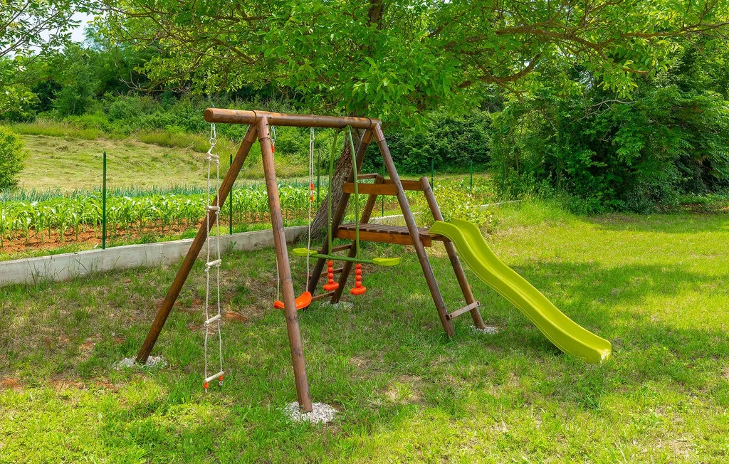 Una estructura de juegos de madera con columpios y un tobogán verde está sobre el césped.