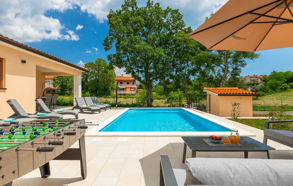 Una piscina al aire libre está junto a un patio embaldosado con asientos y una mesa.