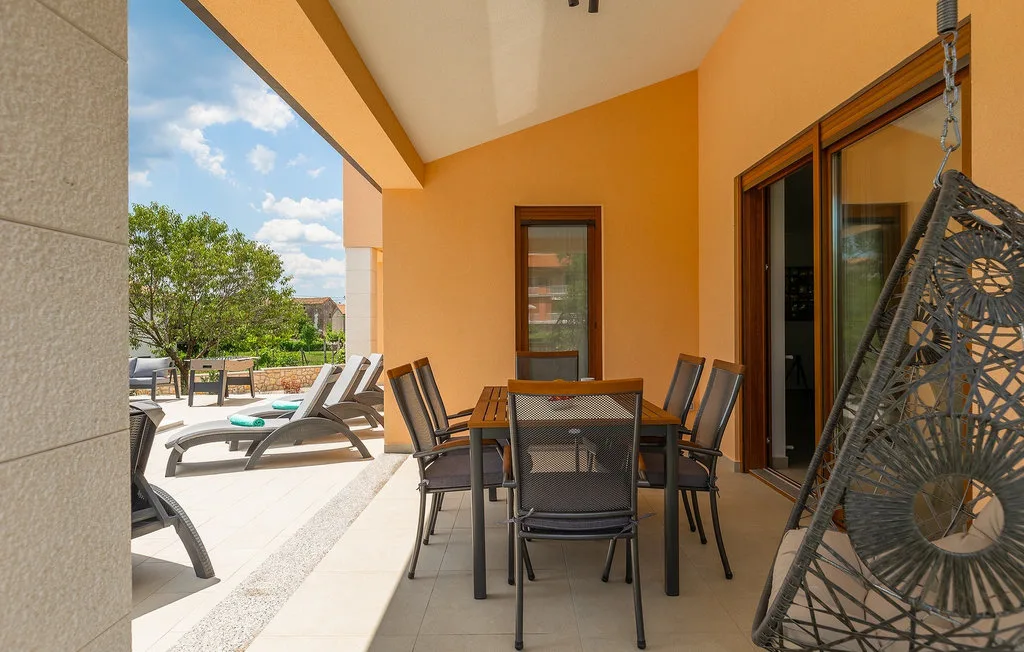 Un patio soleado con asientos para comer al aire libre y sillones junto a la casa.