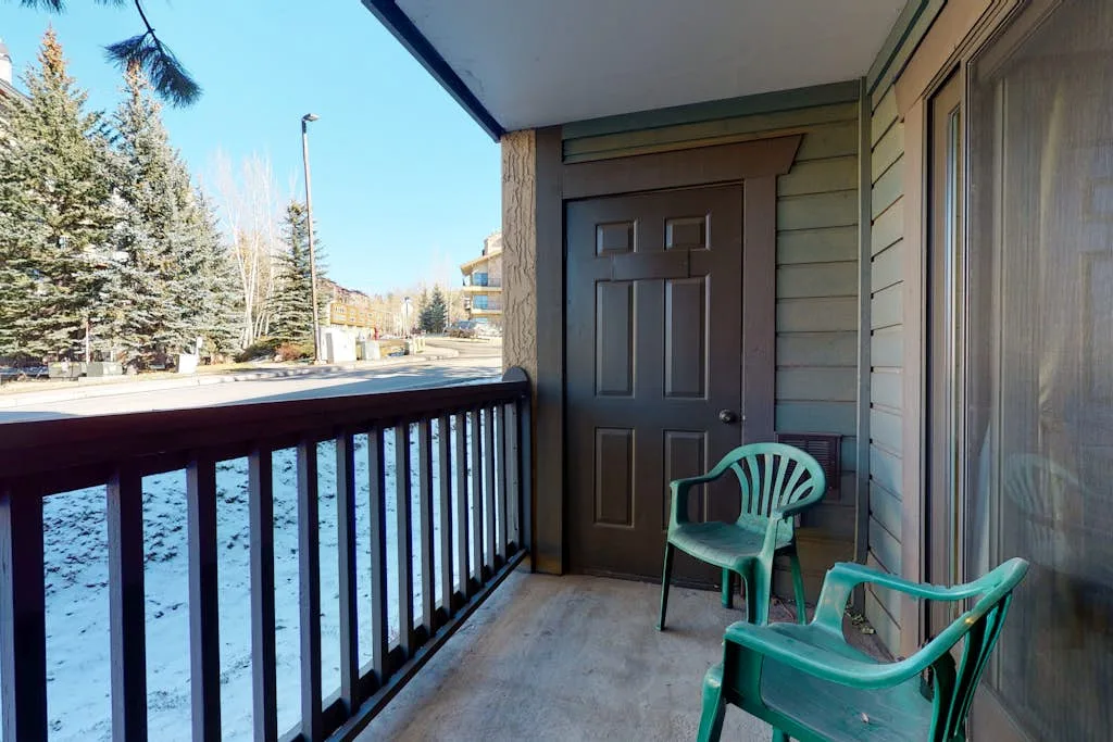 A covered balcony with green seating overlooks a snowy street.