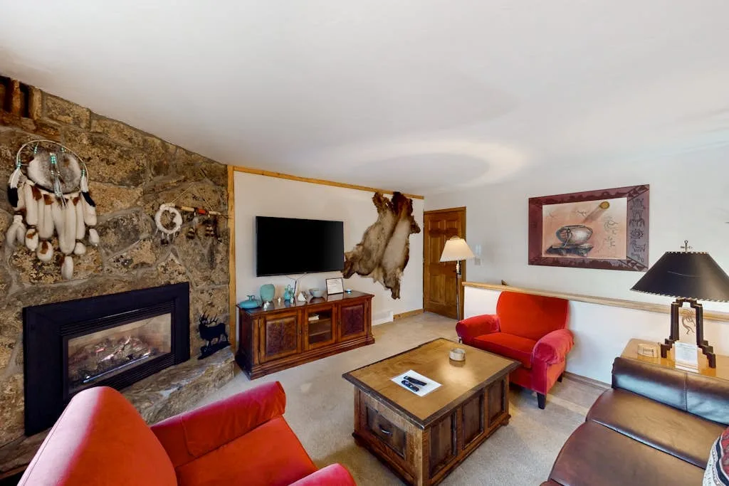 A living room with red seating, a stone fireplace, and a television.