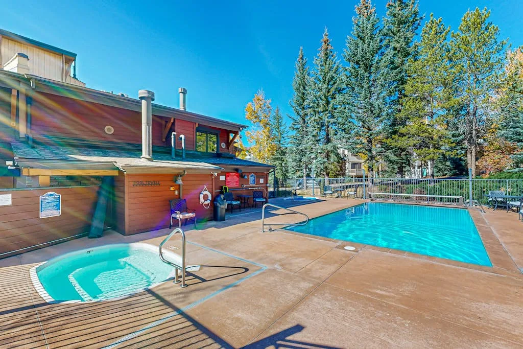 Una piscina al aire libre y una bañera de hidromasaje están junto a un edificio de madera.