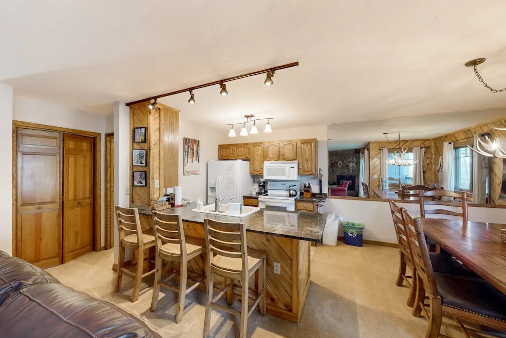 An open-plan kitchen and dining area with a breakfast counter and wooden table.