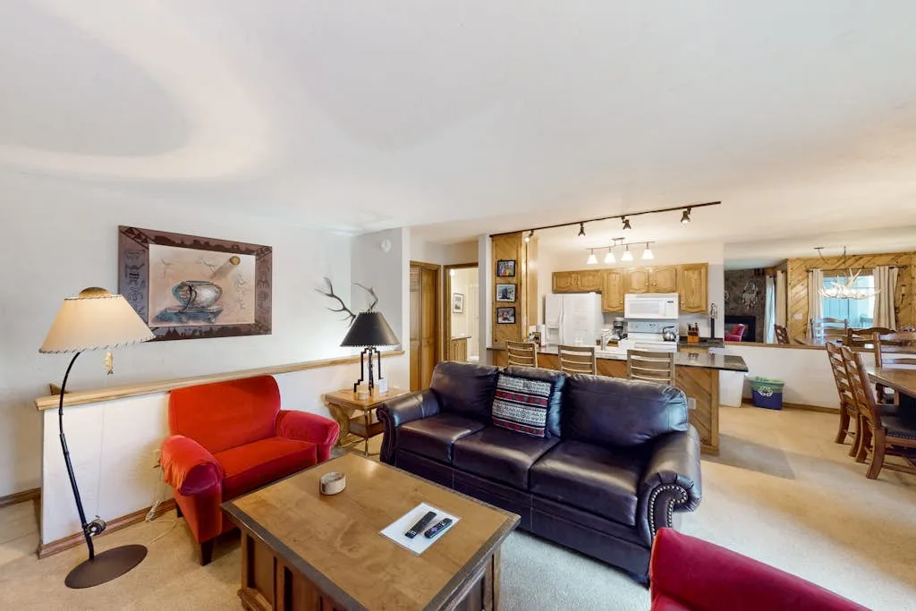 A living room with seating and an open kitchen in the background.