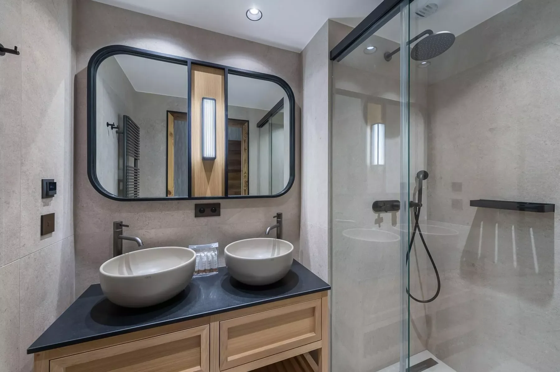 Un baño moderno con dos lavabos sobre encimera y una ducha de vidrio.