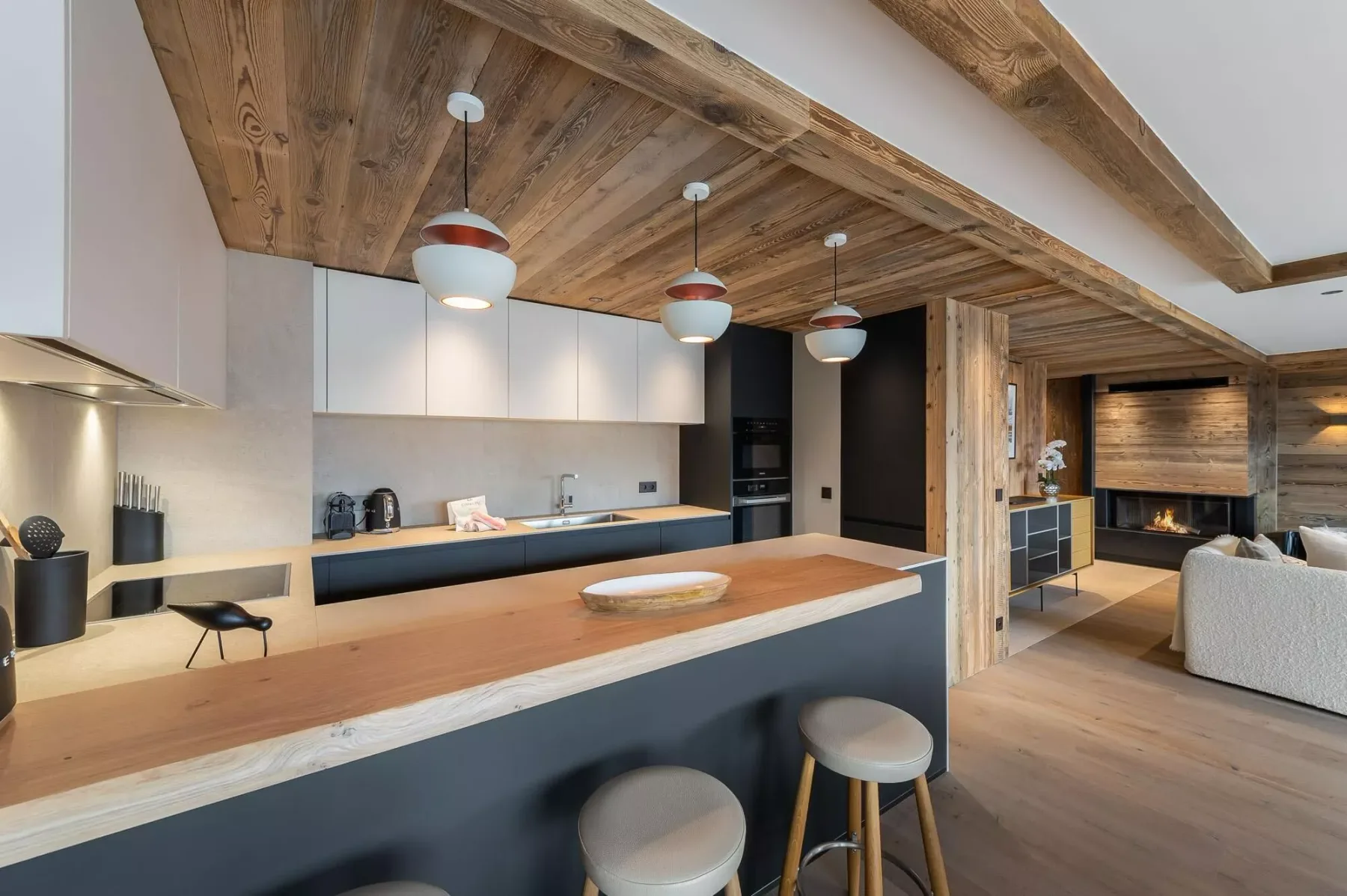 Cocina moderna con una barra larga abierta a una sala de estar con chimenea.