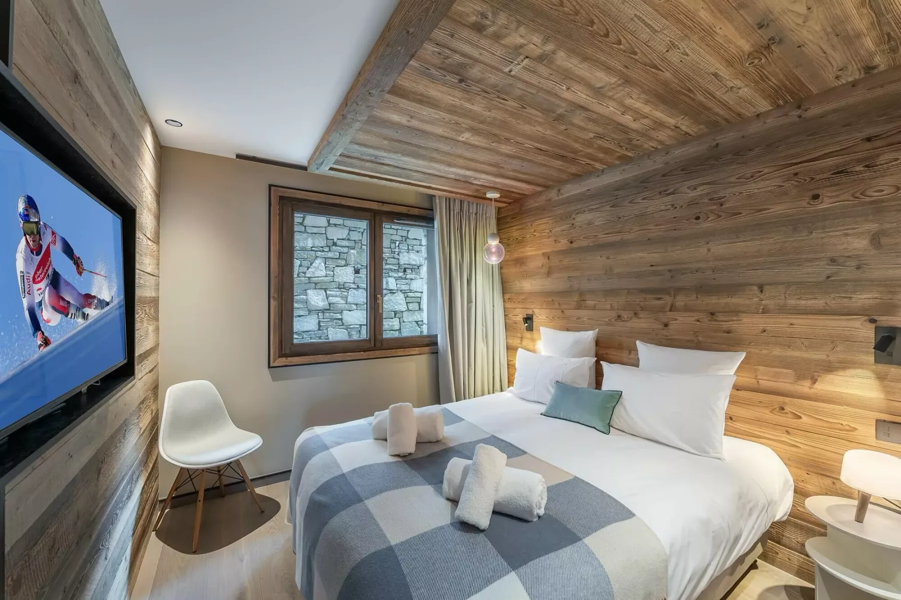 A bedroom with a large bed, wooden walls, and a television.