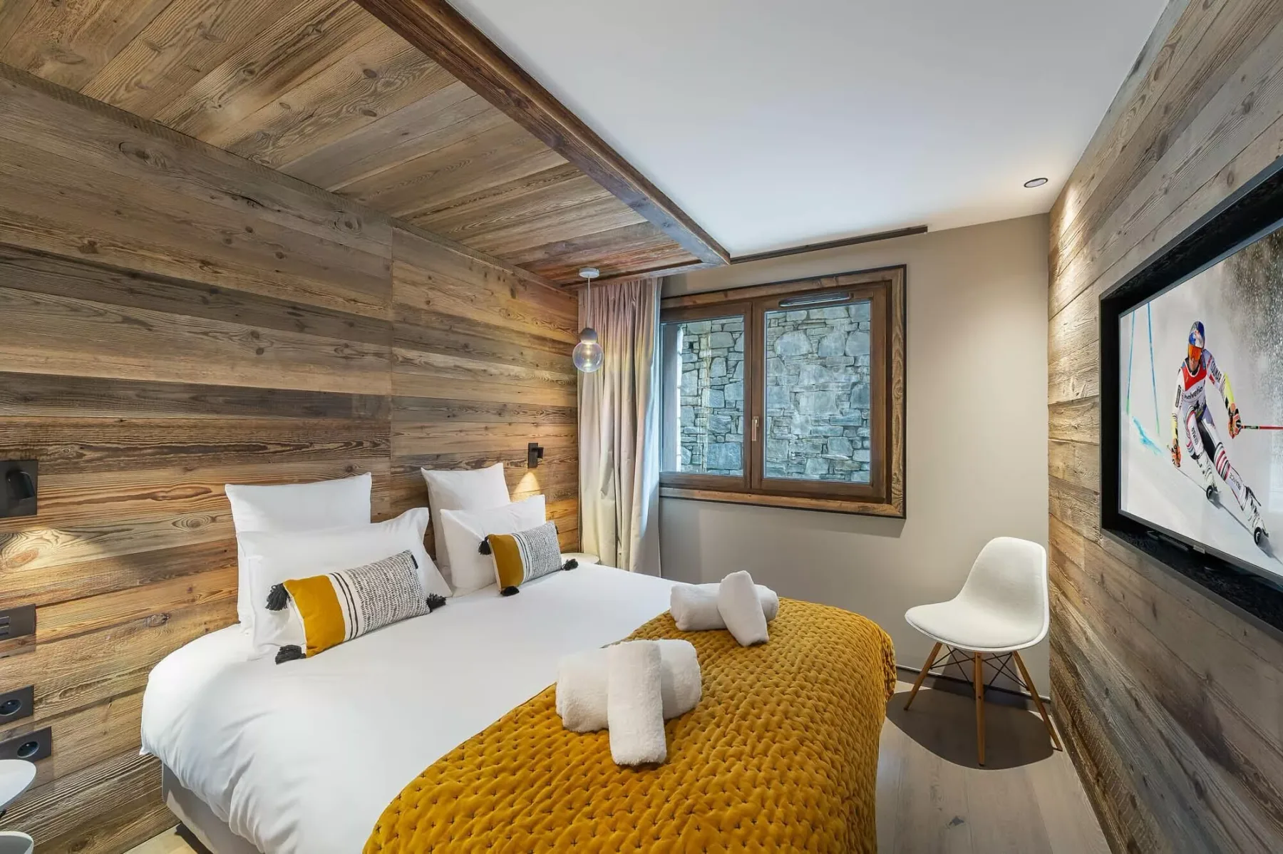 A bedroom with a bed dressed in white linens and a mustard-colored blanket.