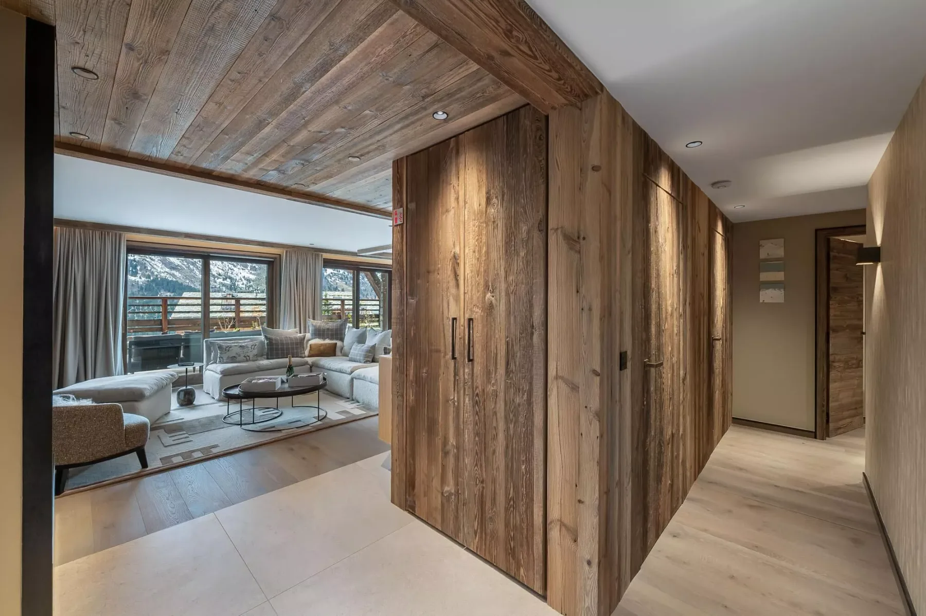 Un pasillo revestido de madera se abre a una sala de estar con asientos y ventanas amplias.