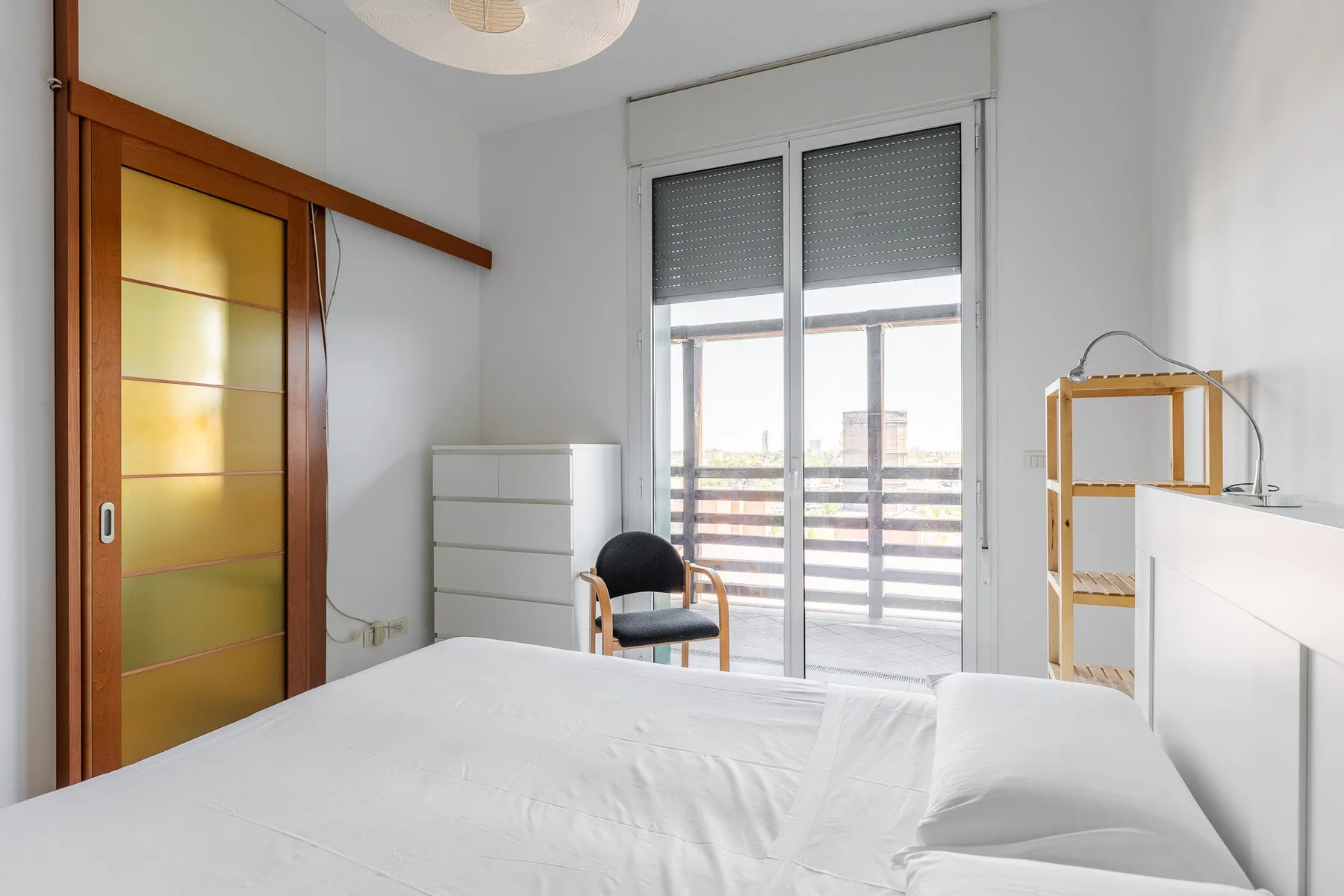 Un dormitorio luminoso con una cama, una puerta corredera de vidrio y una pequeña zona de estar.