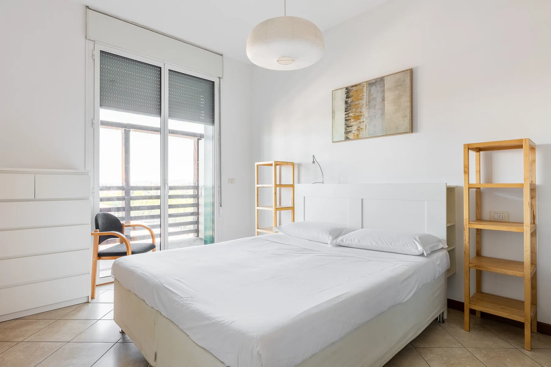 Un dormitorio luminoso con una cama blanca y grandes puertas de vidrio que dan a un balcón.