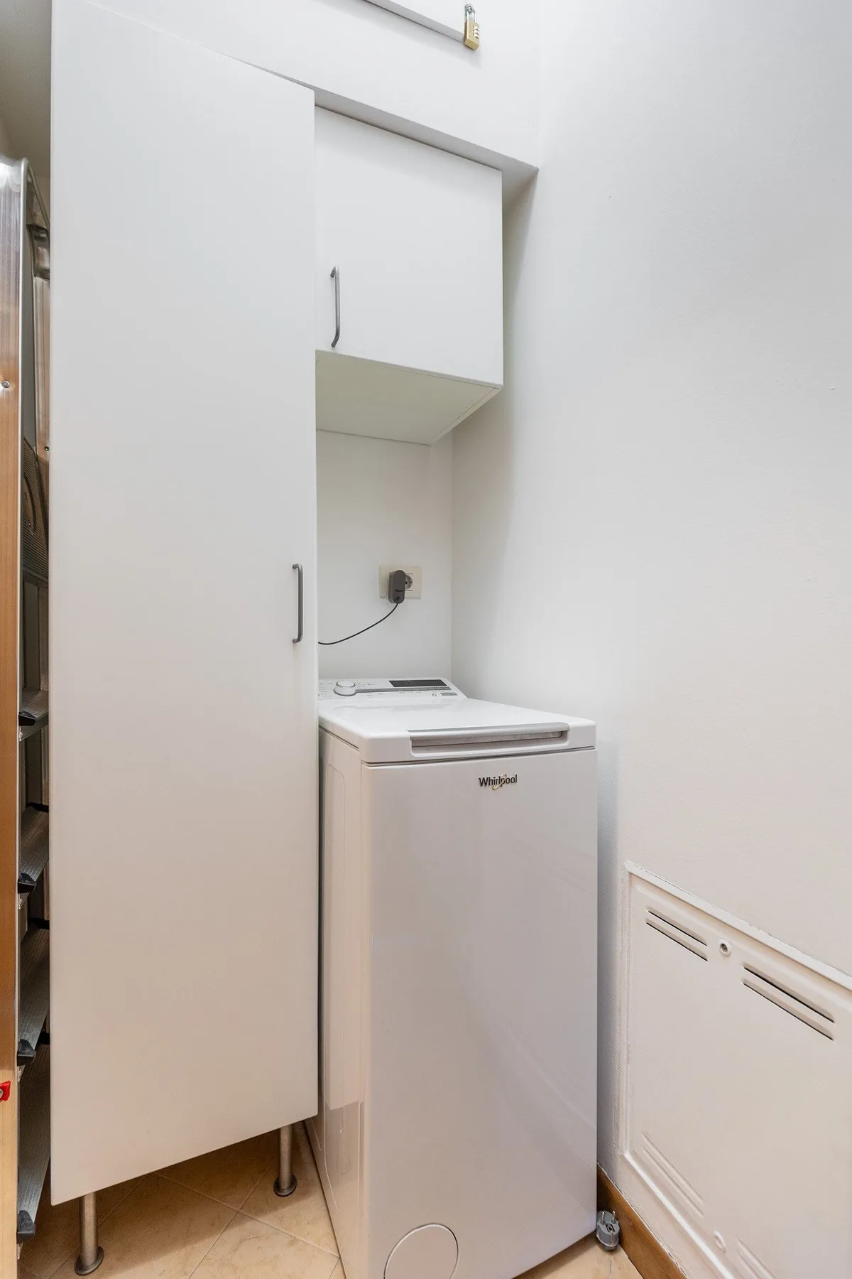 Una pequeña zona de lavandería con una lavadora de carga superior bajo un armario de pared.