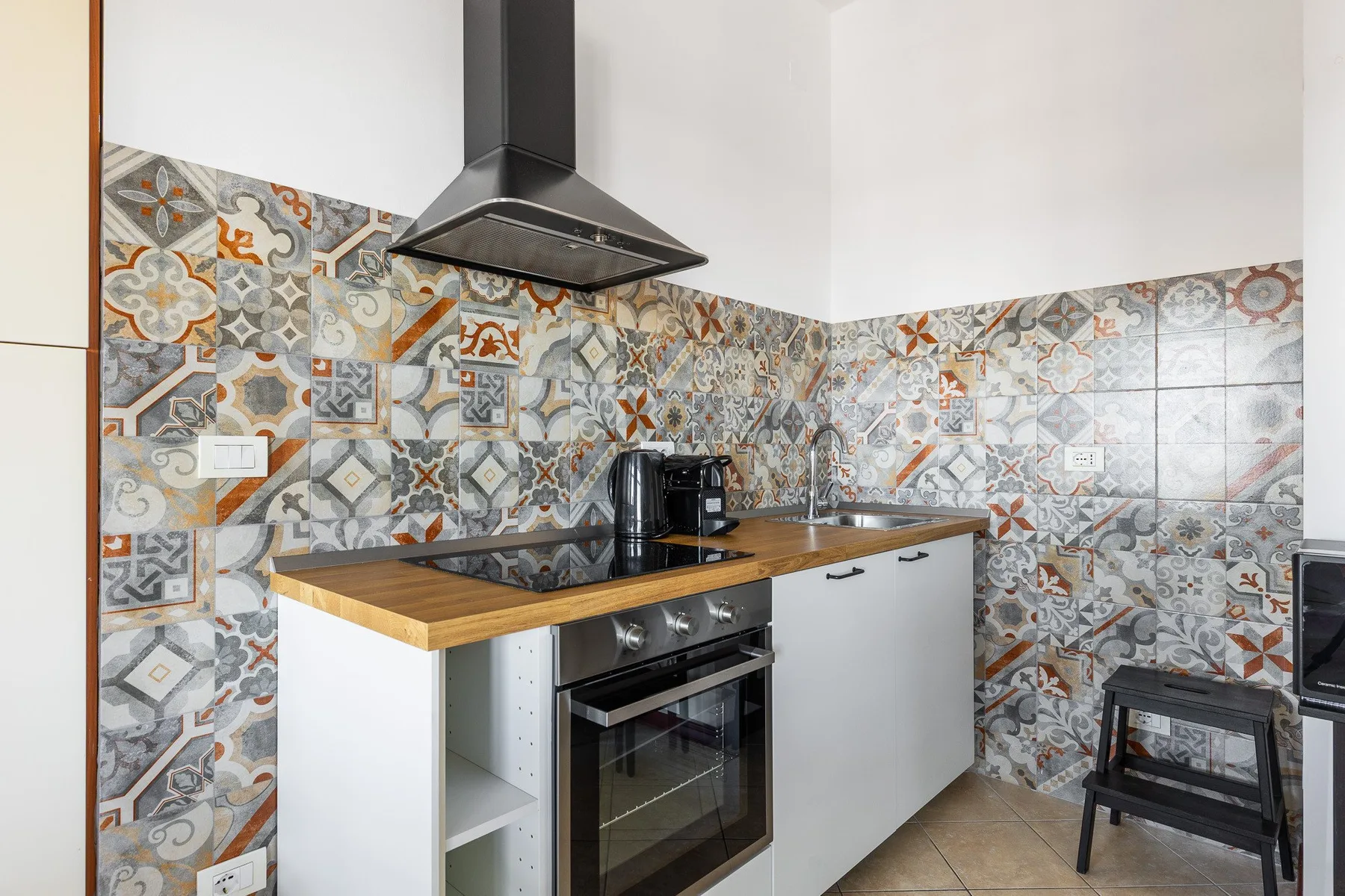 Una cocina compacta con paredes de azulejos estampados, una encimera y un horno empotrado.