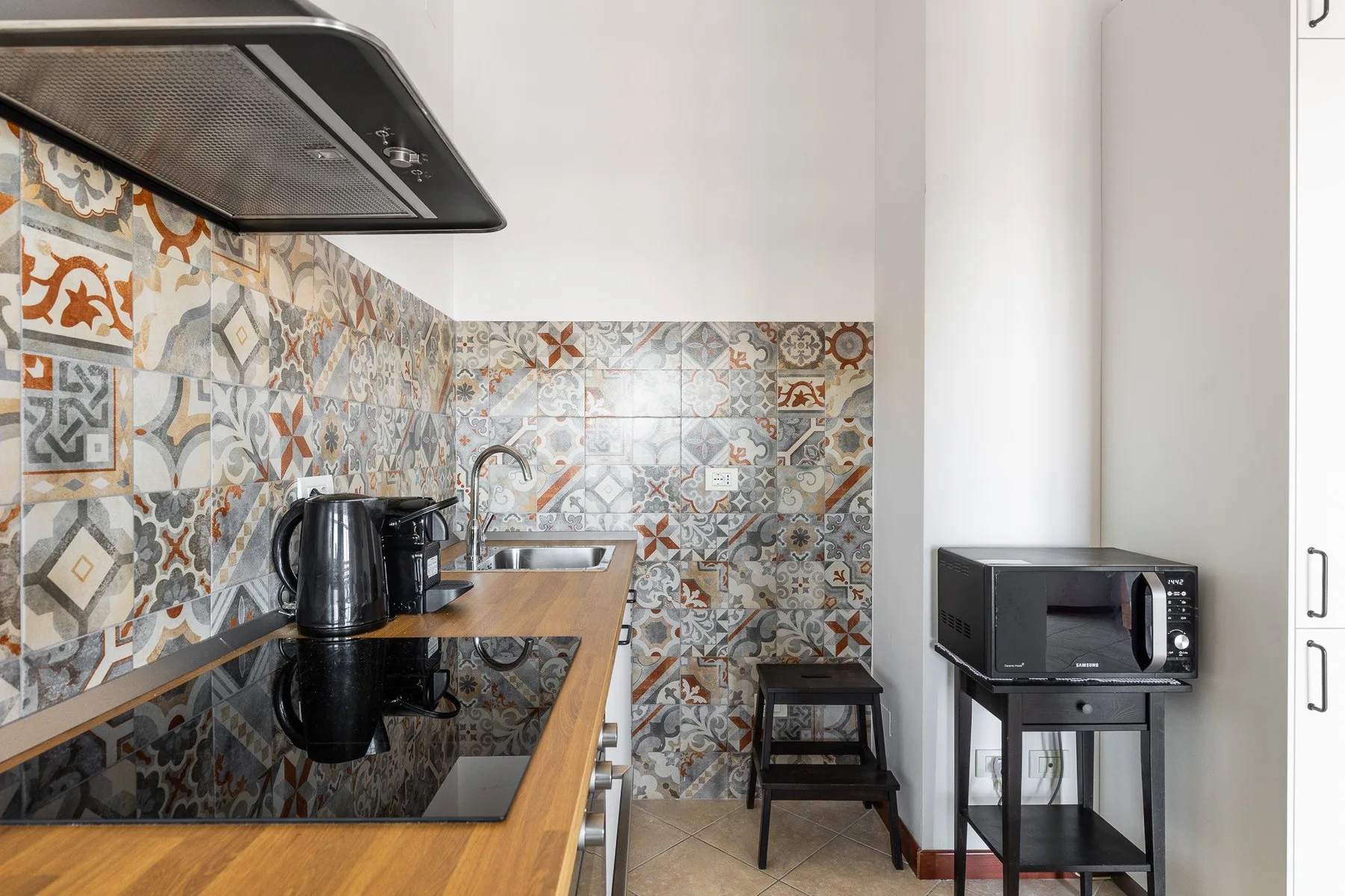 Una cocina compacta con placa de cocción, salpicadero estampado y electrodomésticos sobre la encimera.