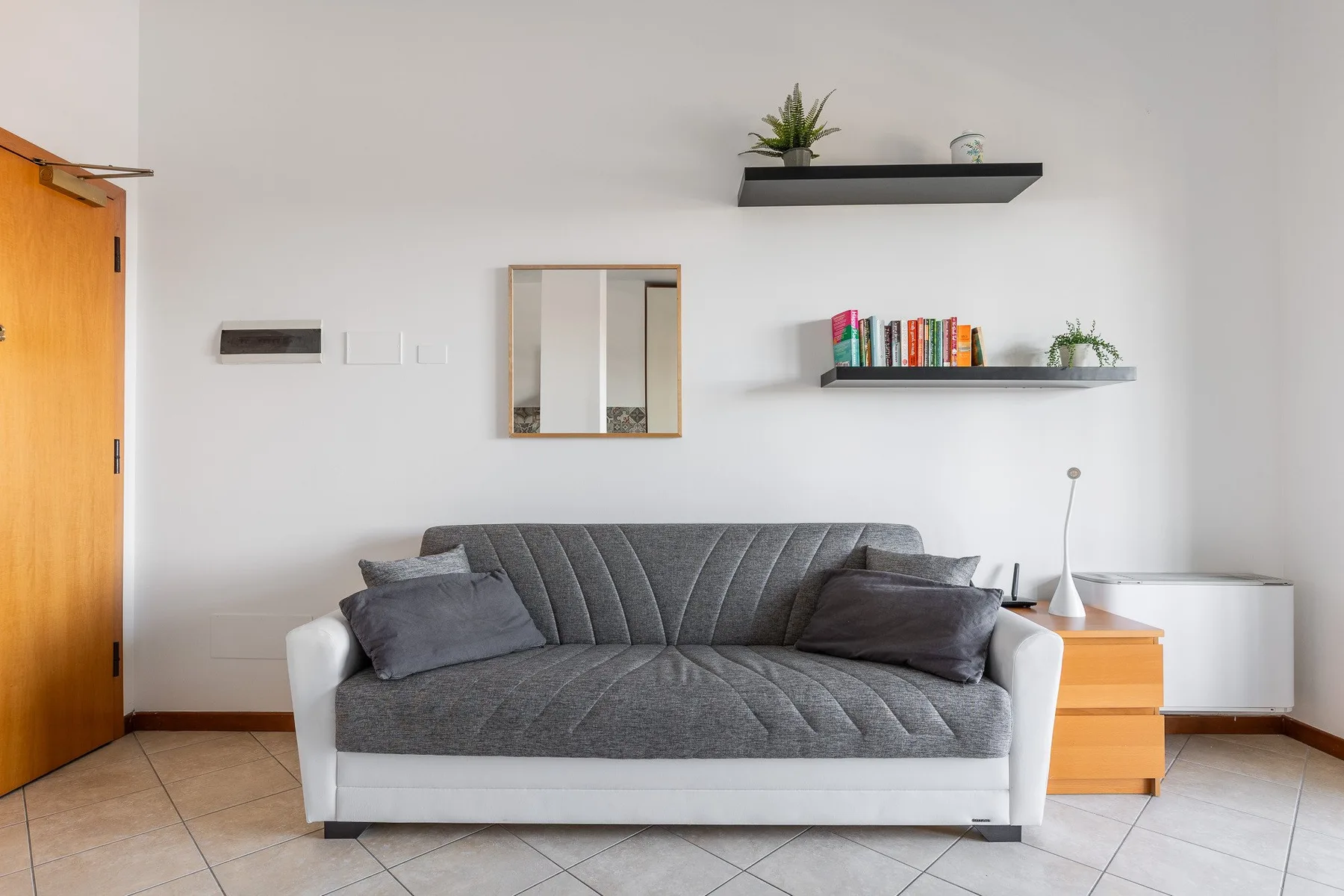 Una sala de estar con un sofá gris debajo de dos estantes de pared.