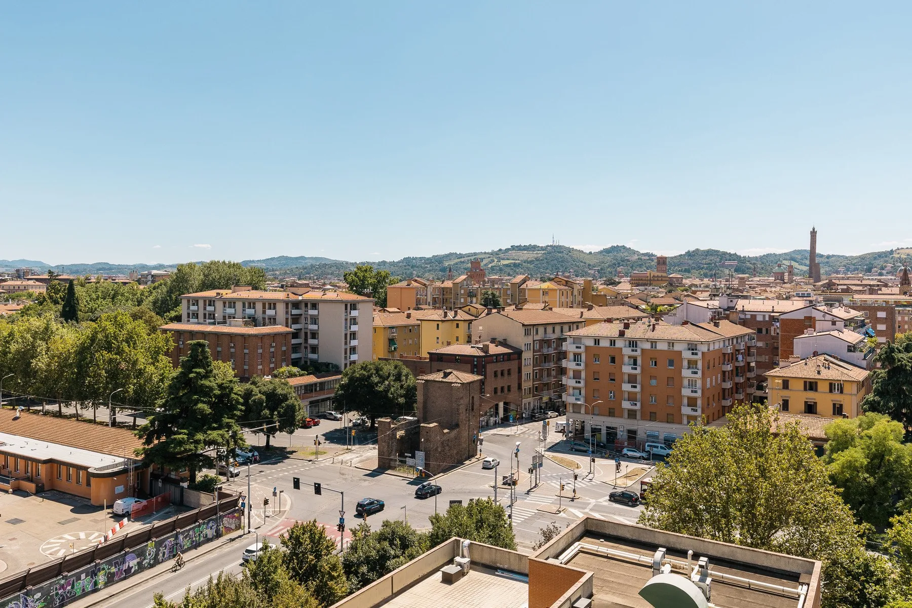 Un paisaje urbano de edificios bajos y calles arboladas bajo colinas lejanas.