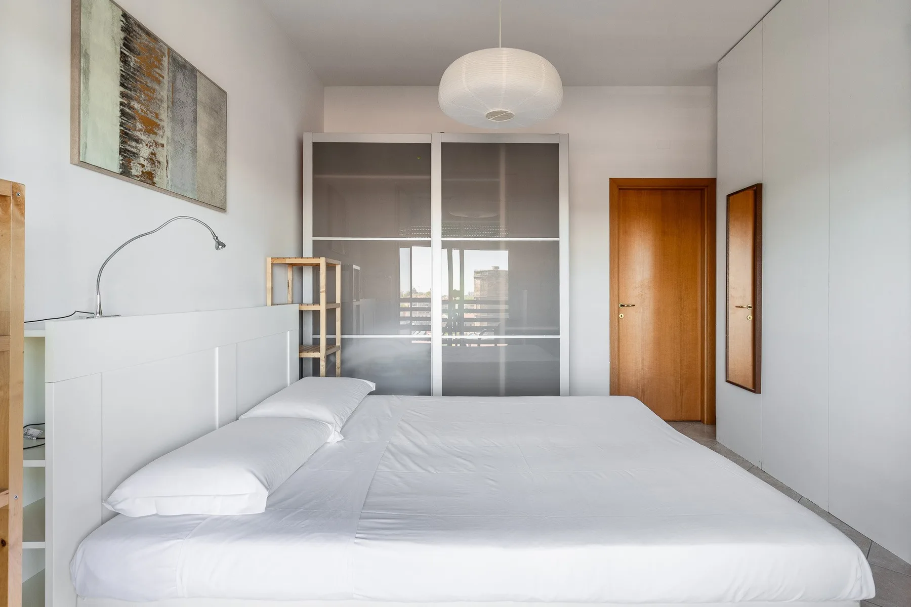 Un dormitorio luminoso con una cama grande blanca y puertas corredizas de vidrio.
