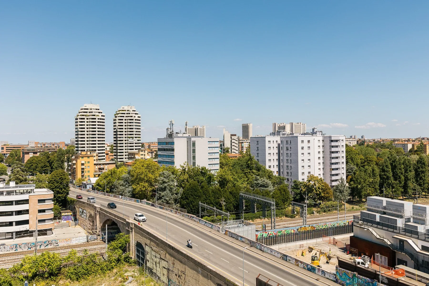 Una vía elevada se curva junto a árboles y edificios en una escena urbana.