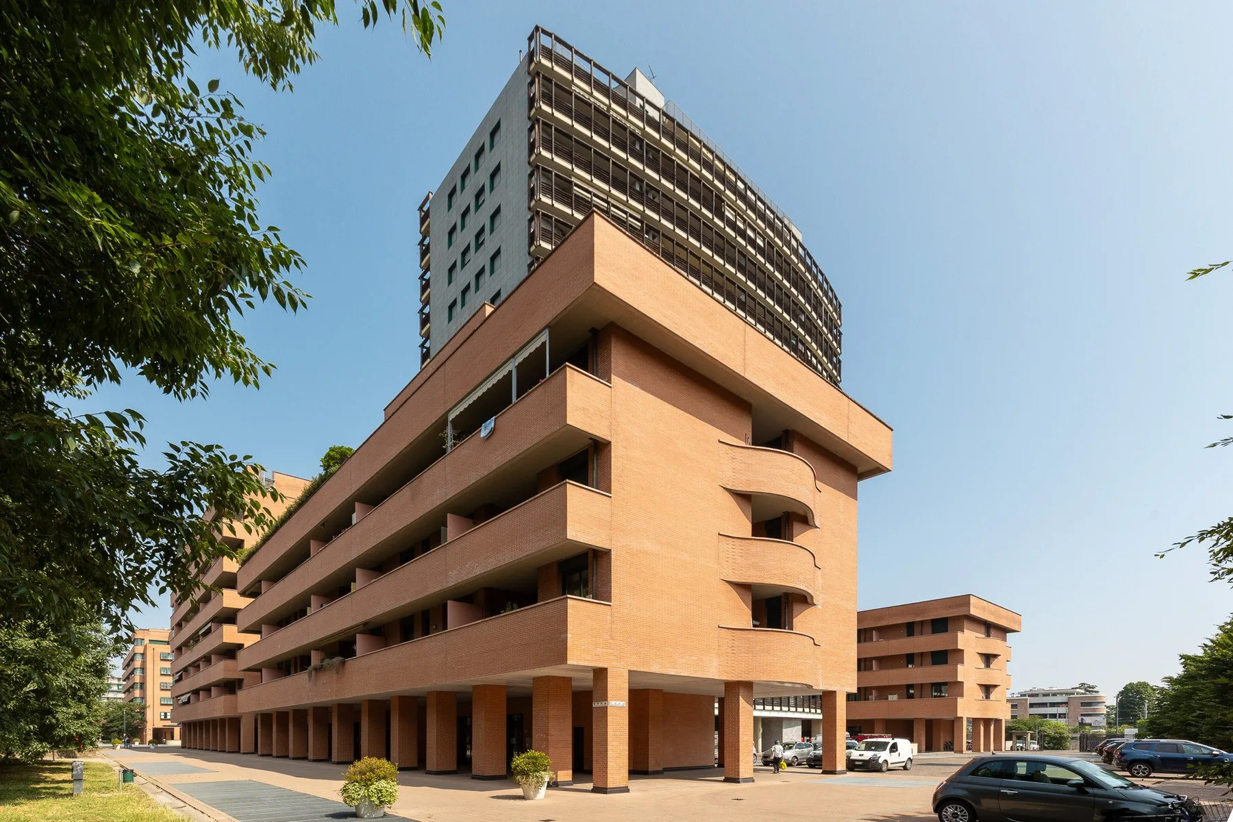 Un edificio de varios pisos con balcones se alza junto a una calle arbolada.