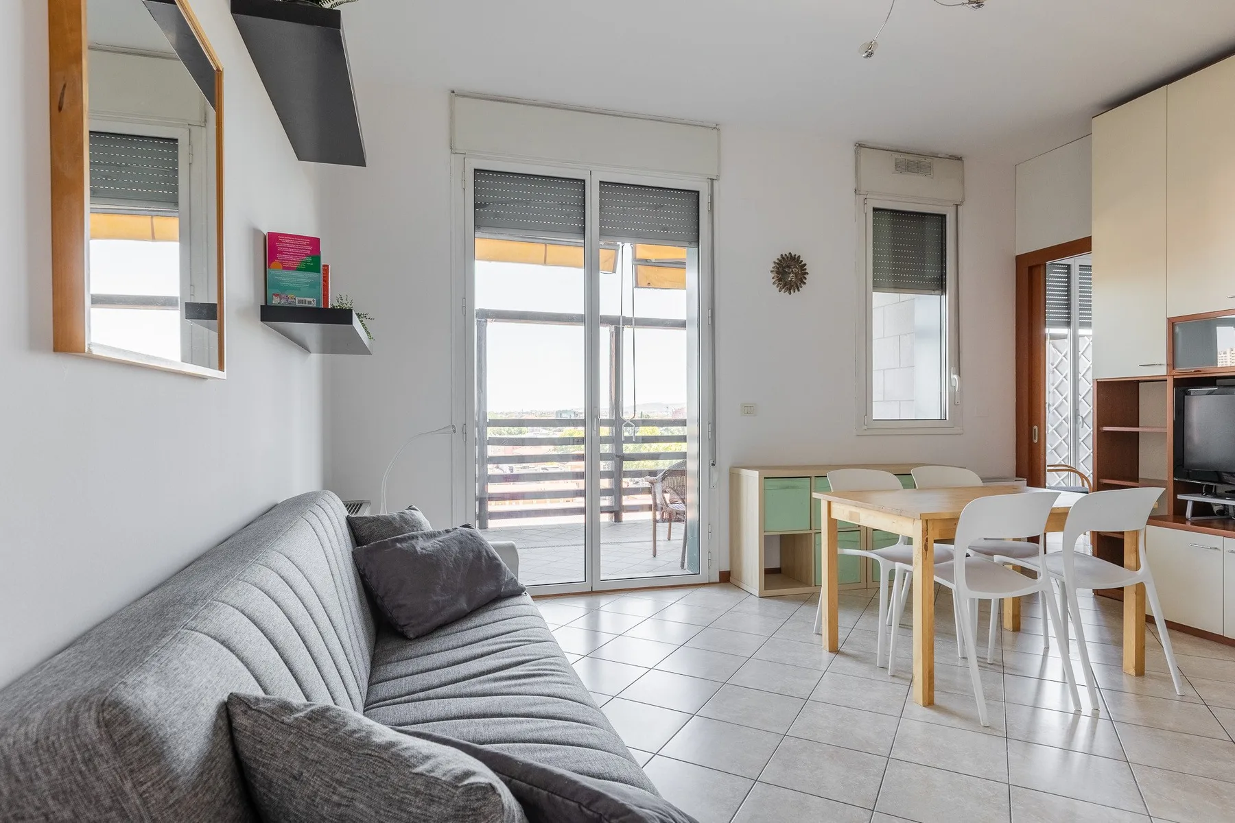 Una luminosa sala de estar y comedor con asientos grises junto a una mesa y puertas al balcón.