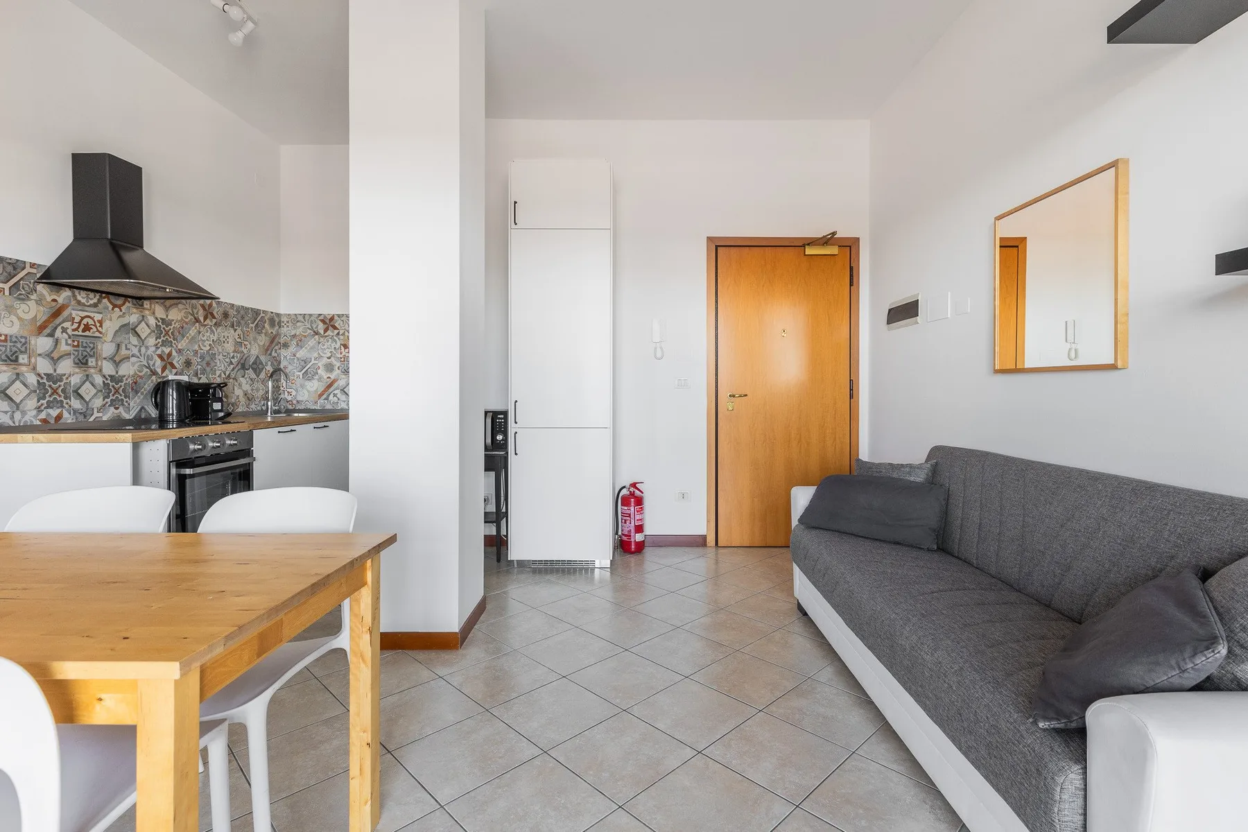 Una luminosa sala-comedor con cocina, mesa de madera y asientos grises.