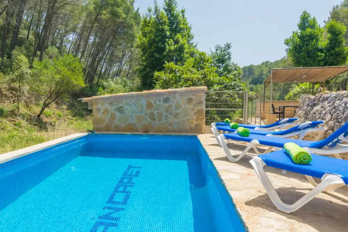 Una piscina al aire libre junto a tumbonas azules y un muro bajo de piedra.