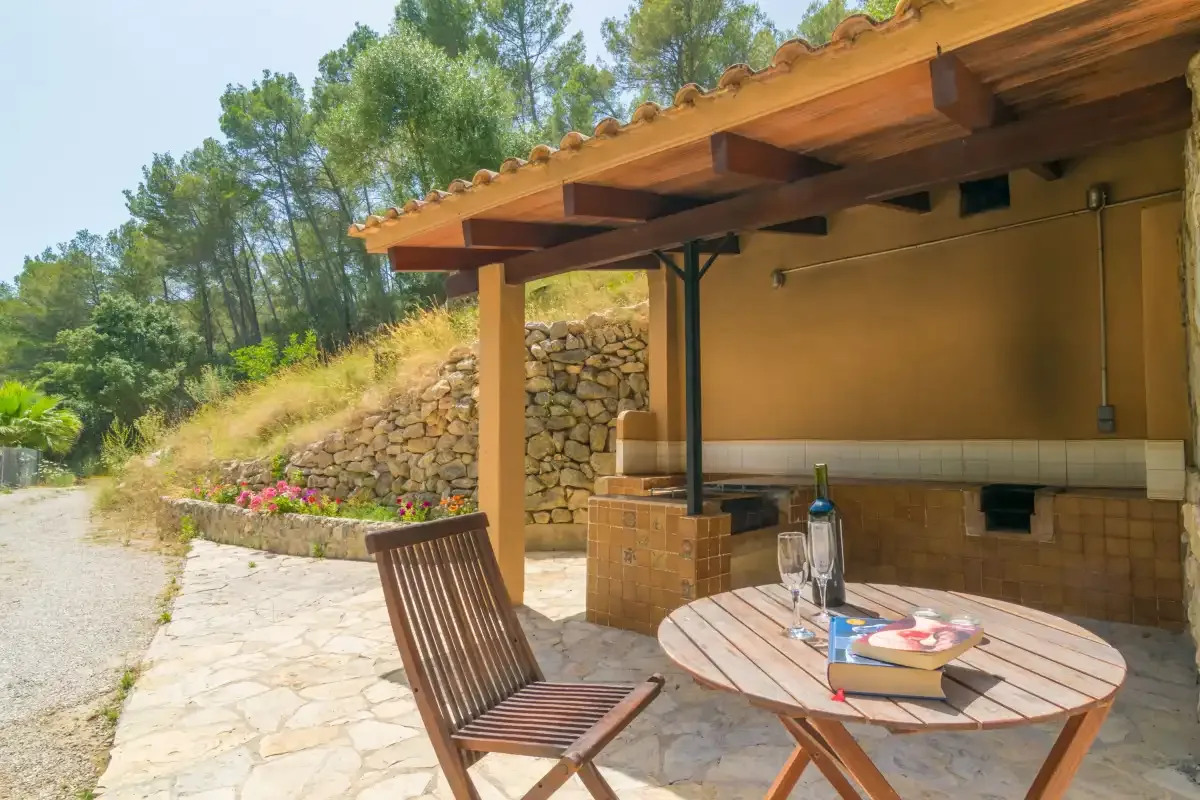Un patio exterior cubierto con una mesa de madera y asientos junto a un muro de piedra.