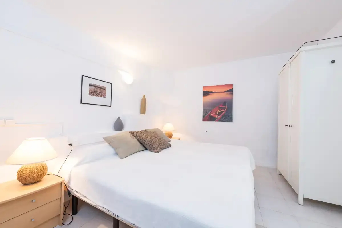 Un dormitorio luminoso con una cama blanca y cuadros enmarcados en la pared.