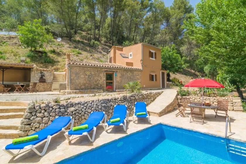 Piscina al aire libre junto a una terraza de piedra con tumbonas y una sombrilla roja.