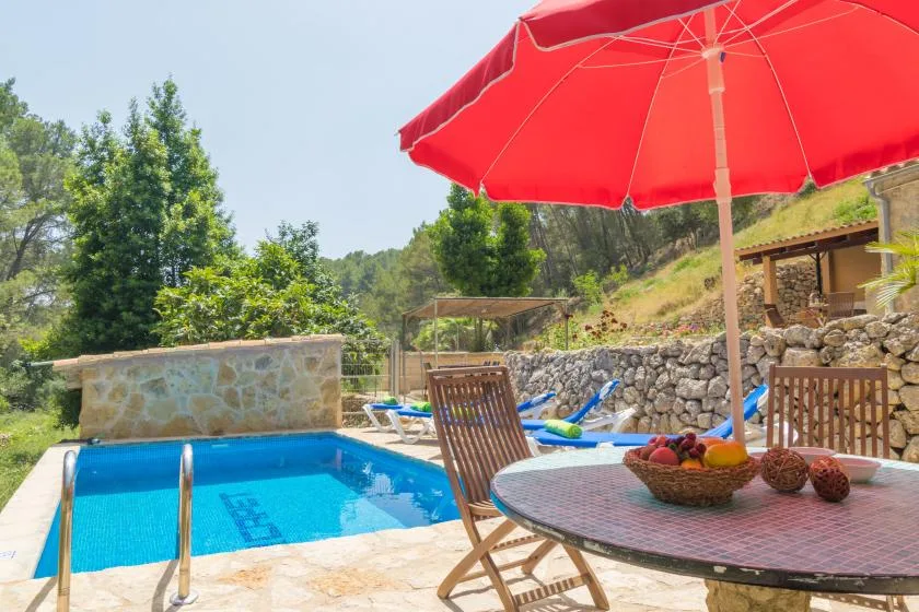 An outdoor swimming pool beside a patio table shaded by a red umbrella.