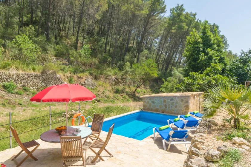 An outdoor swimming pool sits beside a patio with seating and a red umbrella.