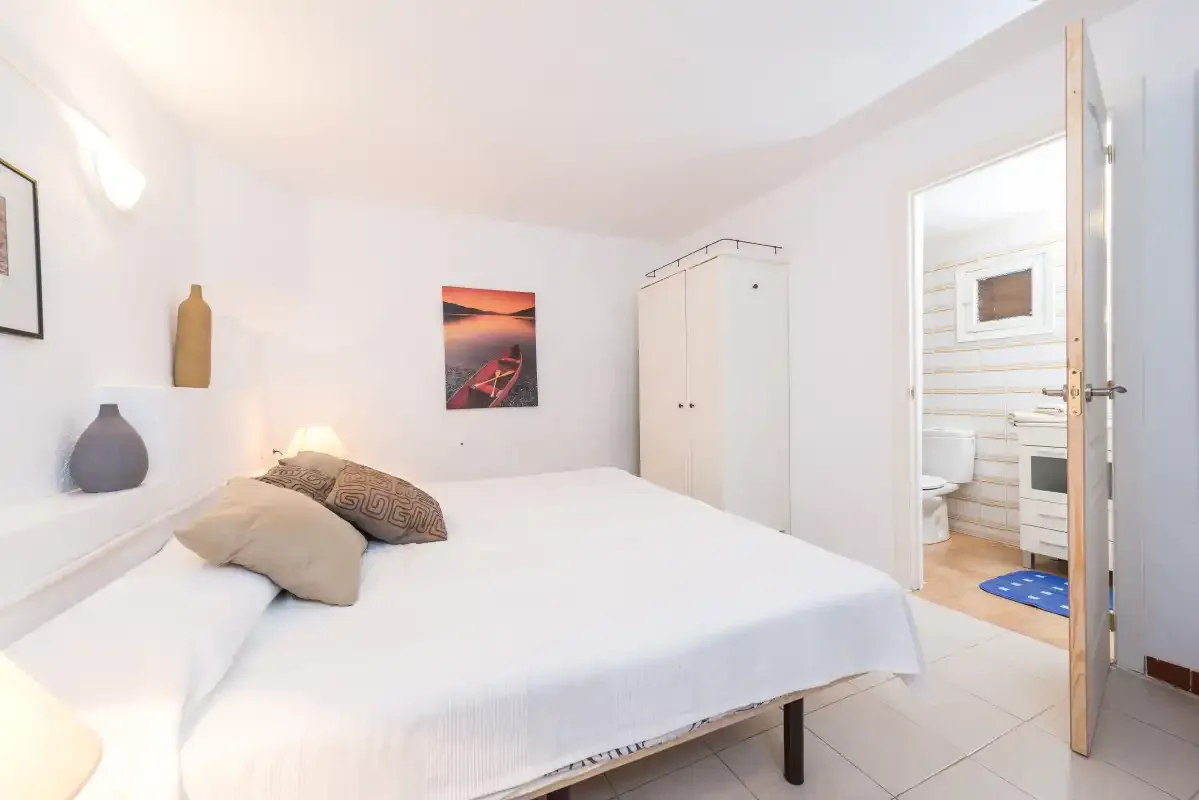 Un dormitorio luminoso con una cama bien hecha y un armario blanco.