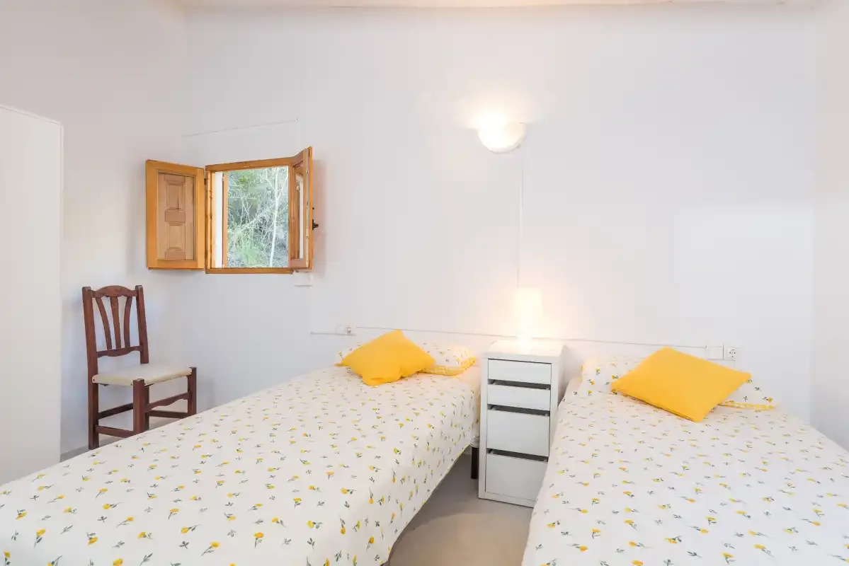 Un dormitorio luminoso tiene dos camas con ropa de cama estampada y almohadas amarillas.