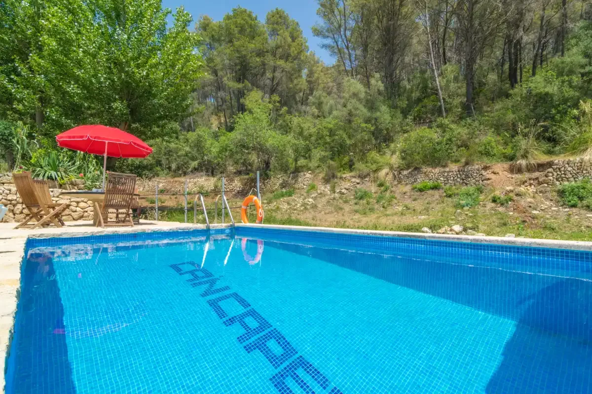 Una piscina al aire libre está junto a una ladera arbolada y una zona de descanso.