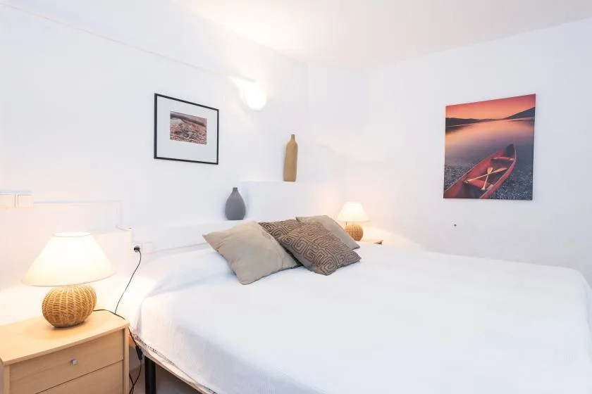 Un dormitorio luminoso con una cama bien tendida y cuadros en las paredes.