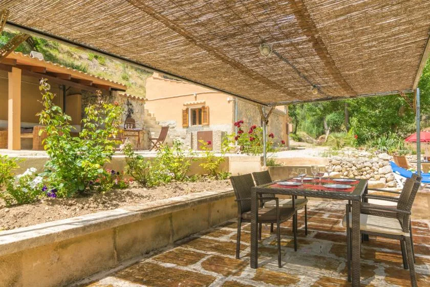 Una zona de comedor al aire libre está bajo una cubierta de sombra junto a un jardín.