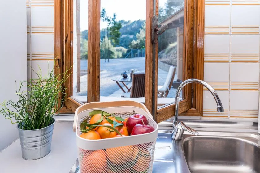Un fregadero y una encimera de cocina están junto a una ventana con vista a asientos exteriores.