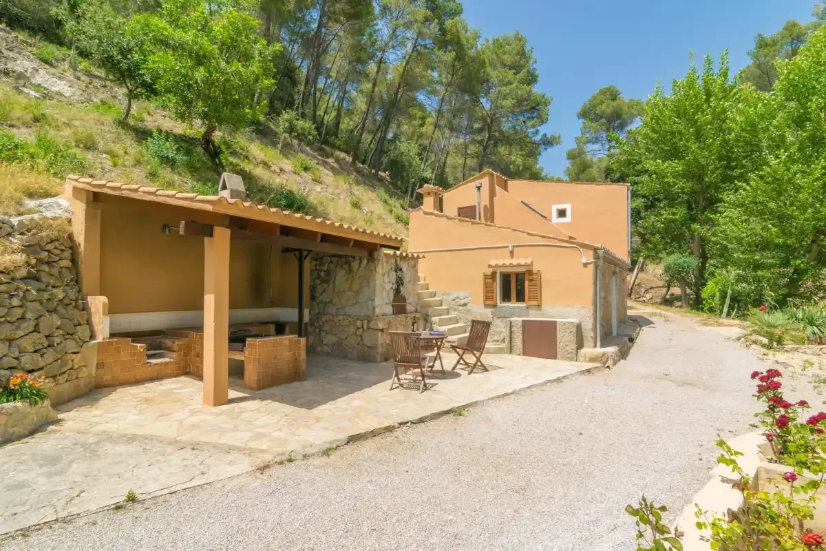 Un patio de piedra junto a una casa, con una zona de estar cubierta.