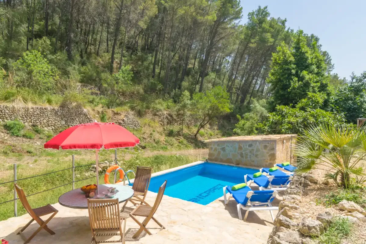 Una piscina al aire libre junto a un patio con asientos y una sombrilla roja.