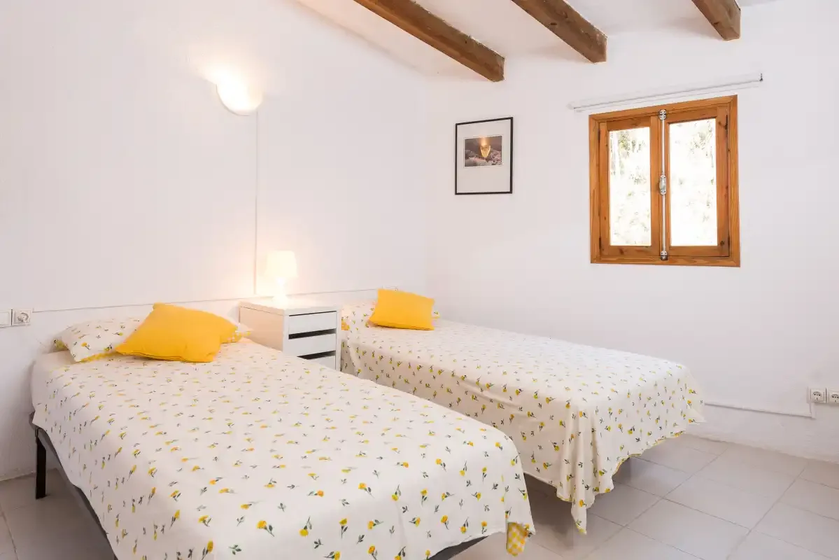 Un dormitorio luminoso con dos camas individuales y una ventana con marco de madera.