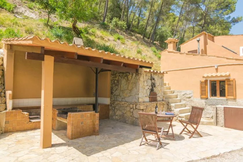 Un patio de piedra soleado con una zona de cocina exterior cubierta y asientos.