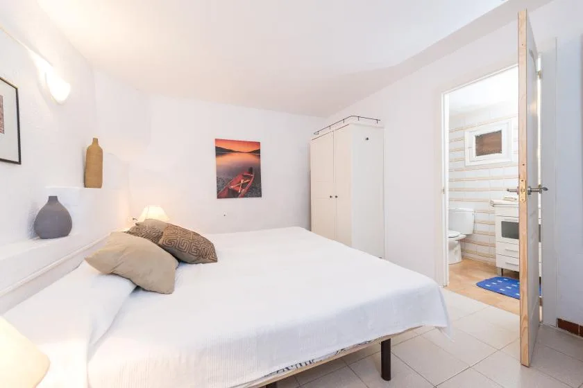 Un dormitorio luminoso con una cama grande y una puerta abierta a un baño con azulejos.
