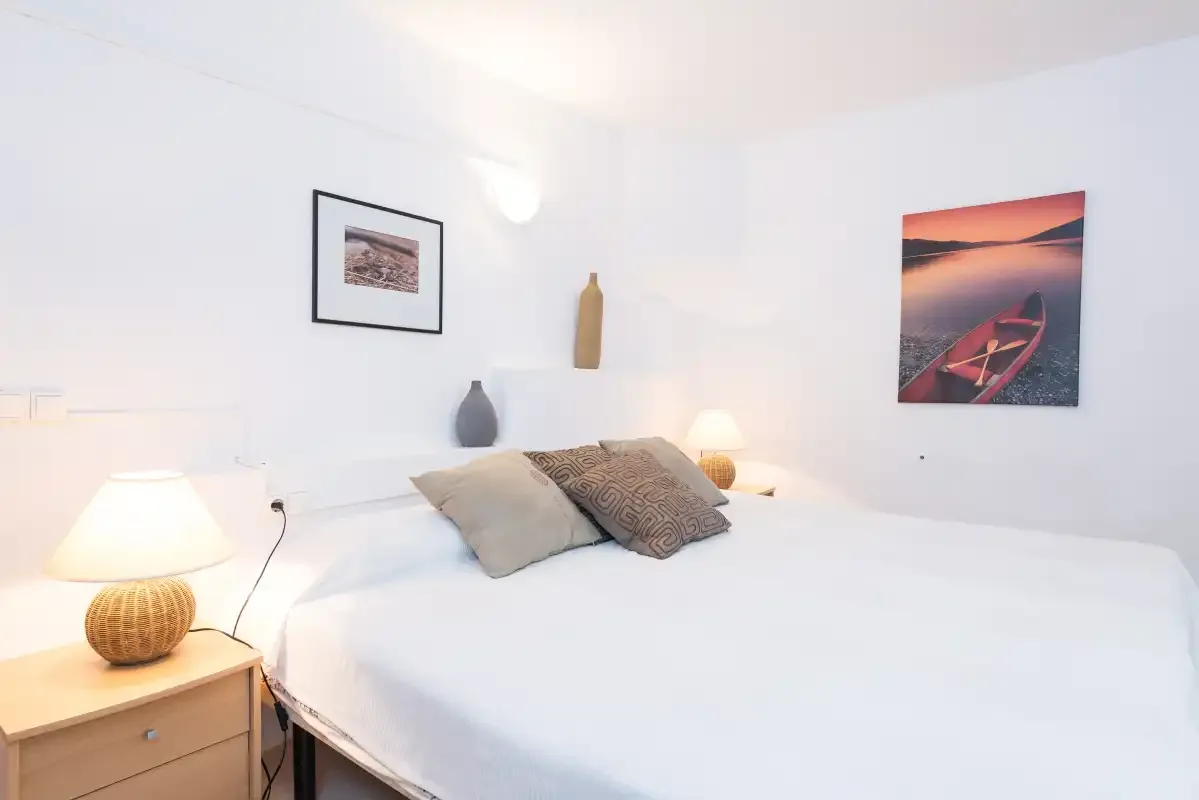 Un dormitorio luminoso con una cama bien tendida y cuadros en la pared.