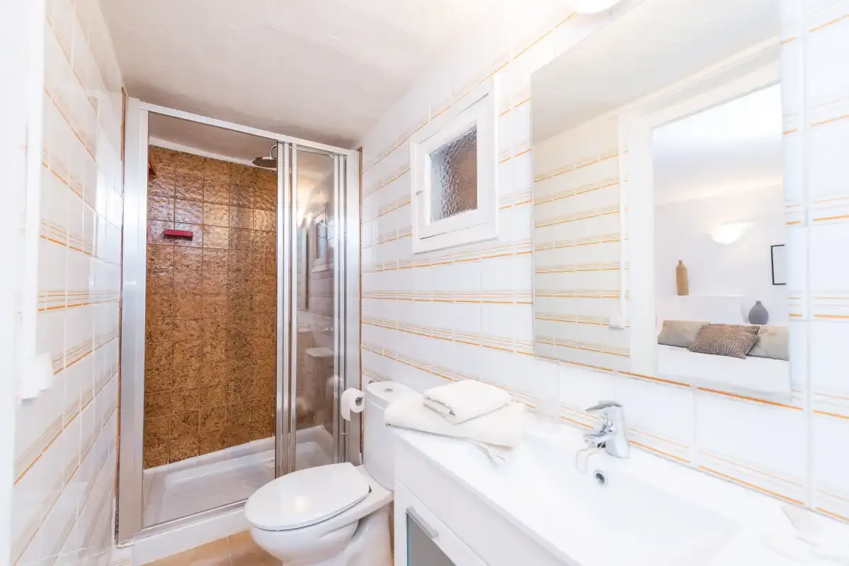 Un baño con inodoro, lavabo y ducha con mampara de vidrio.