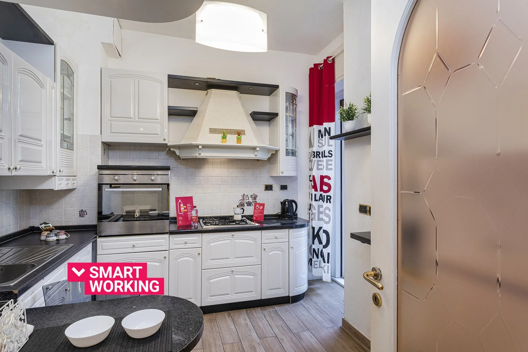 Una cocina luminosa con armarios blancos, encimeras oscuras y una zona de cocción central.