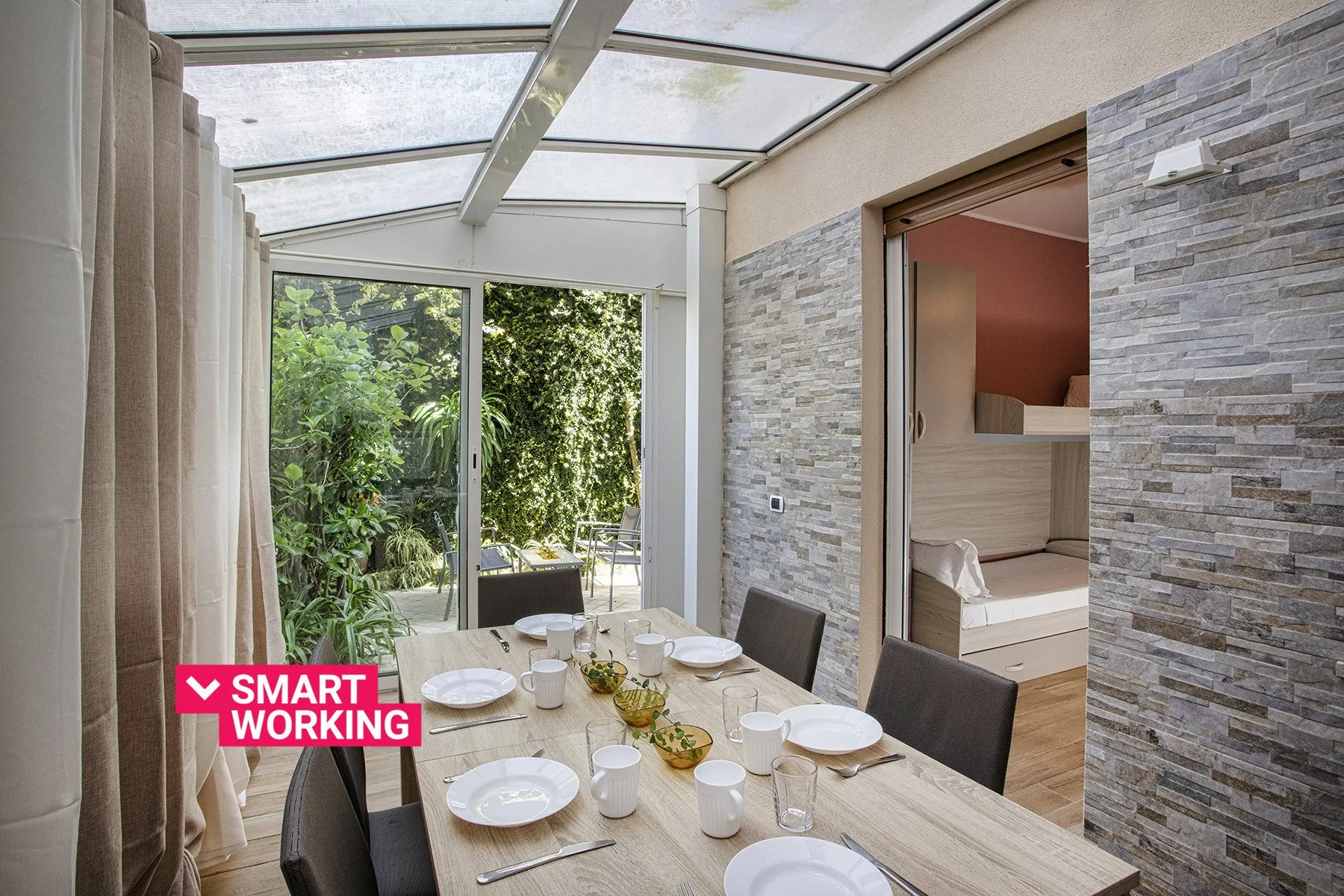 Un comedor bajo un techo de cristal, con una mesa junto a grandes ventanas.