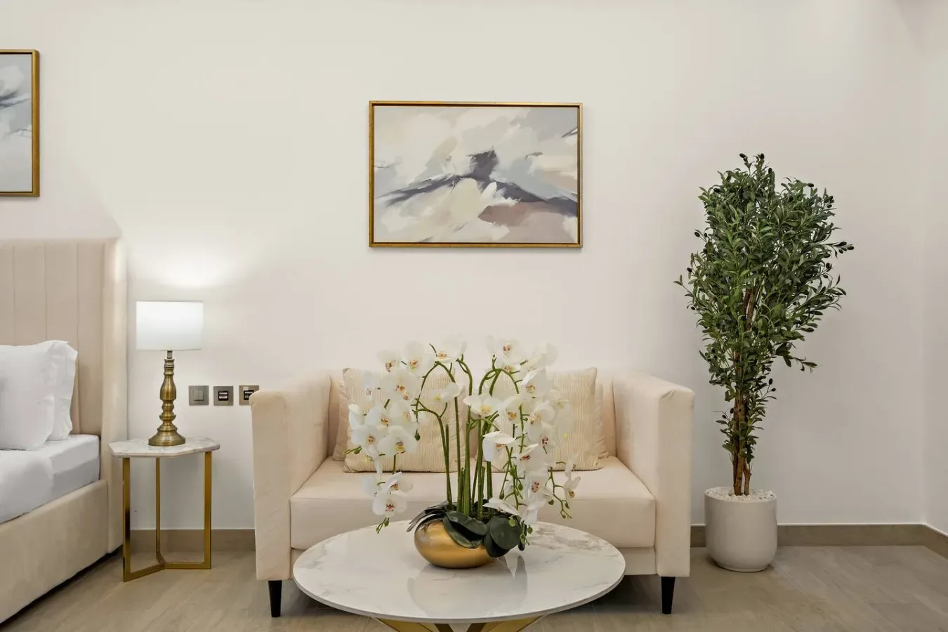 Una sala de estar amueblada en tonos suaves, con un sofá crema, orquídeas y un árbol en maceta.