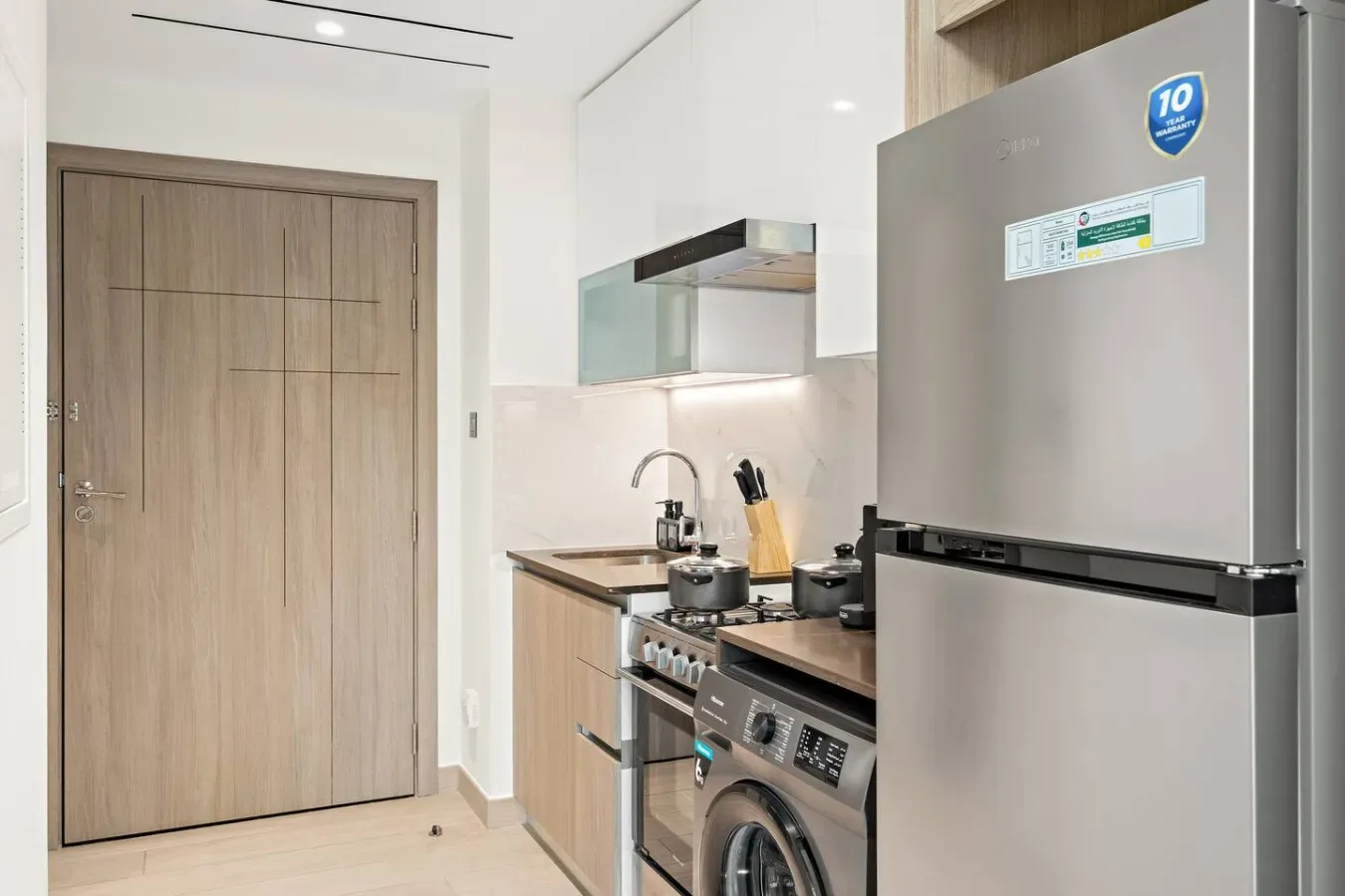 Una cocina compacta con armarios de madera, un refrigerador y una lavadora.
