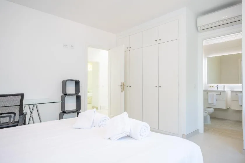 Un dormitorio luminoso con una cama blanca y armarios empotrados.