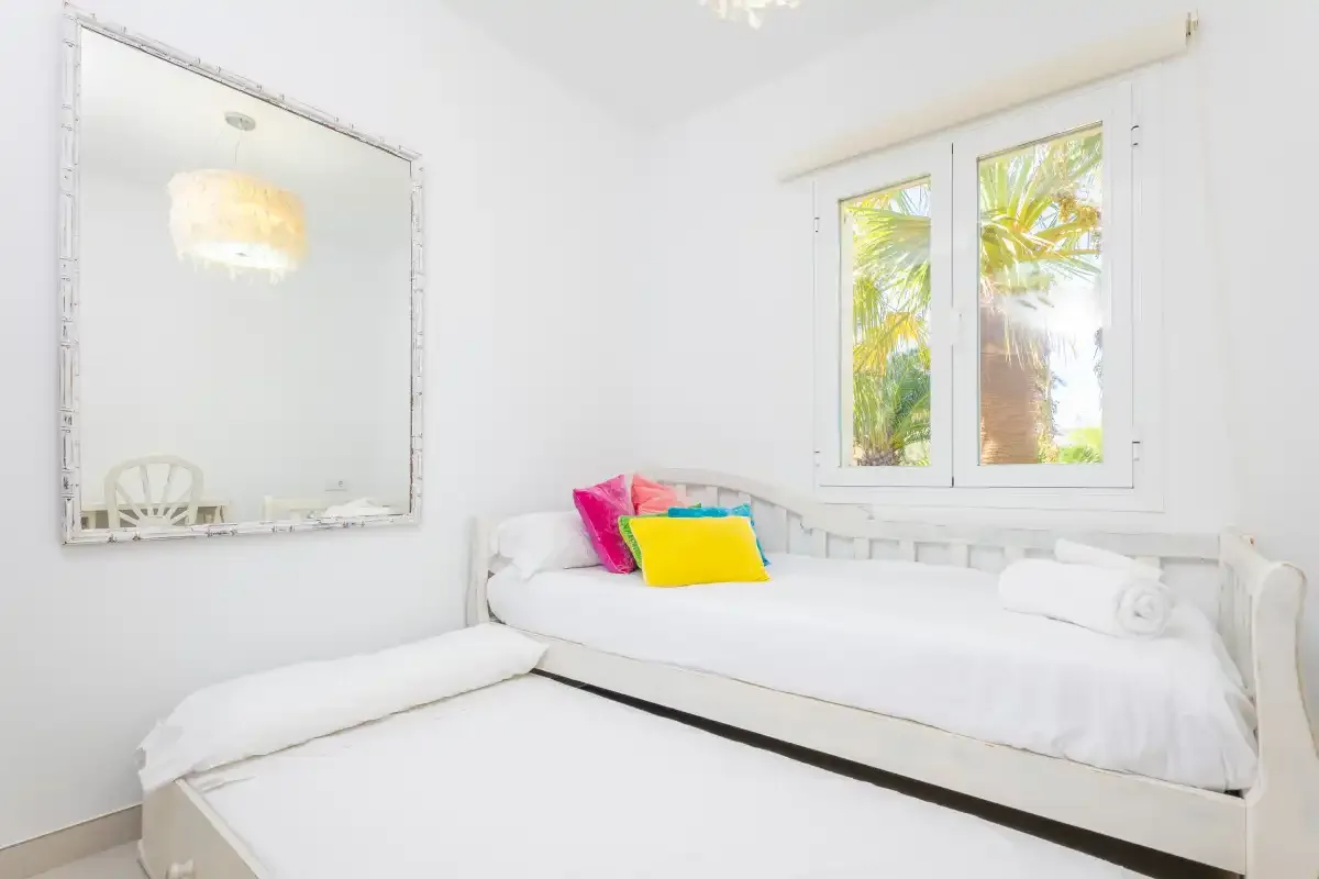 Un dormitorio luminoso con ropa de cama blanca y cojines de colores.